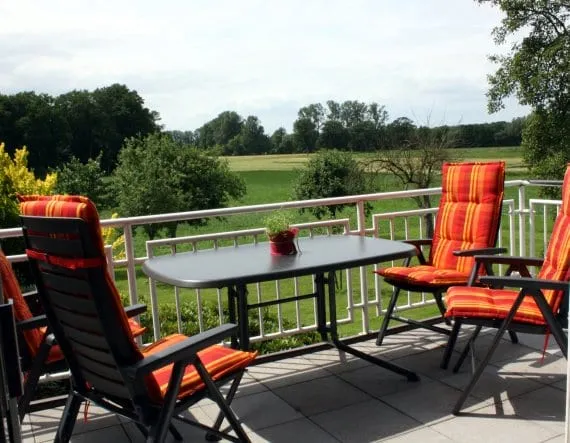 Balkon mit Tisch und Liegestühlen, dahinter Wiesen, Felder und Waldrand