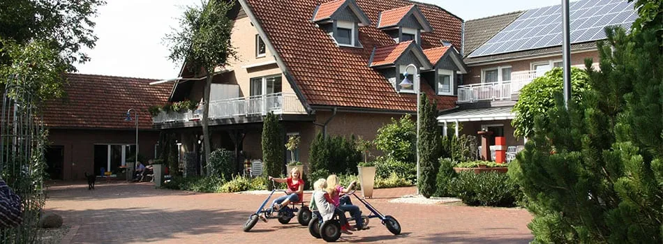 Kinder auf Kettcars vor dem Ferienhaus mit rotem Dach und Balkonen