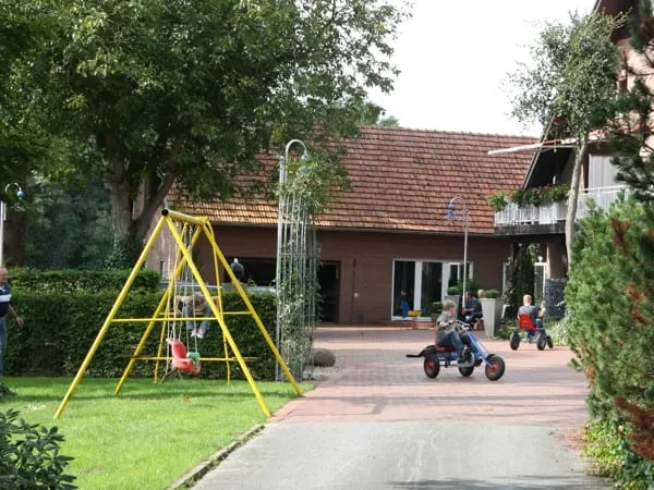 Schaukel und Kinder mit Kettcars auf dem Hof vor dem Backsteinhaus