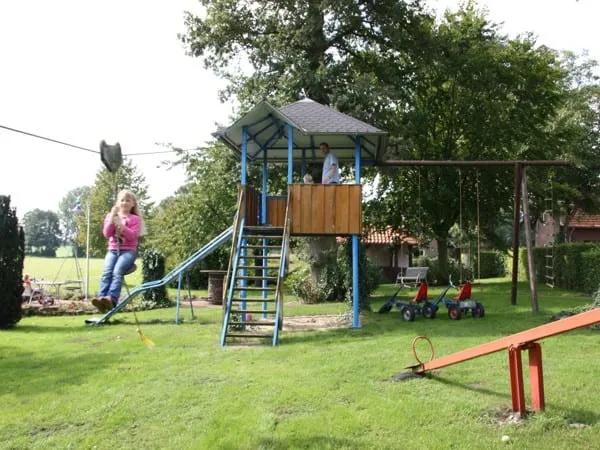 Spielplatz mit Kletterturm, Rutsche, Schaukel und Wippe auf grüner Wiese